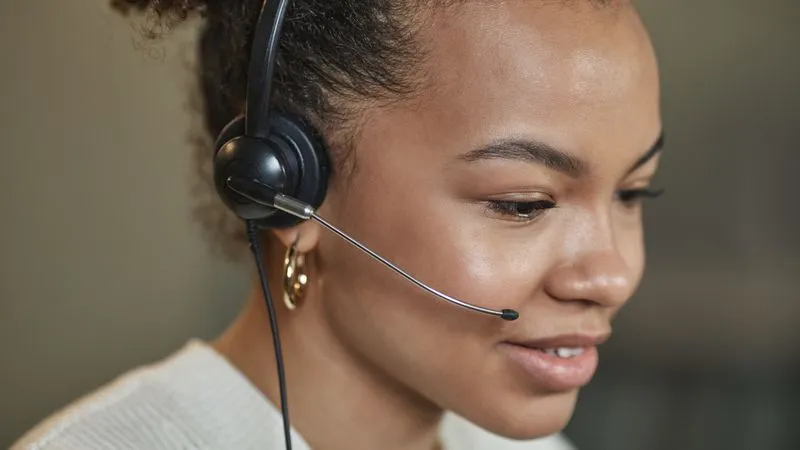 A smiling woman wearing a headset with a microphone looks down while working.