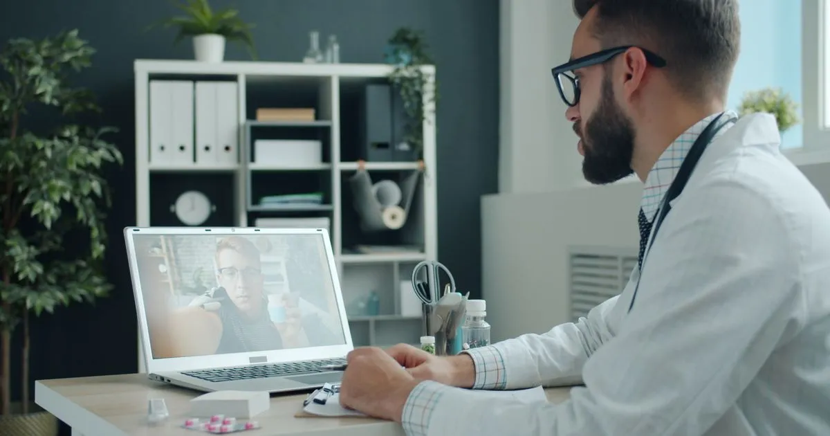 Doctor in a white coat talks with a patient holding a pill bottle on a laptop video call.
