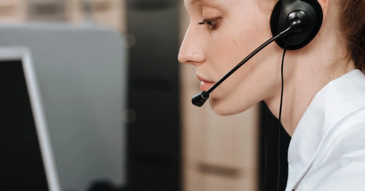 A woman wearing a headset with a microphone looks toward a computer monitor.
